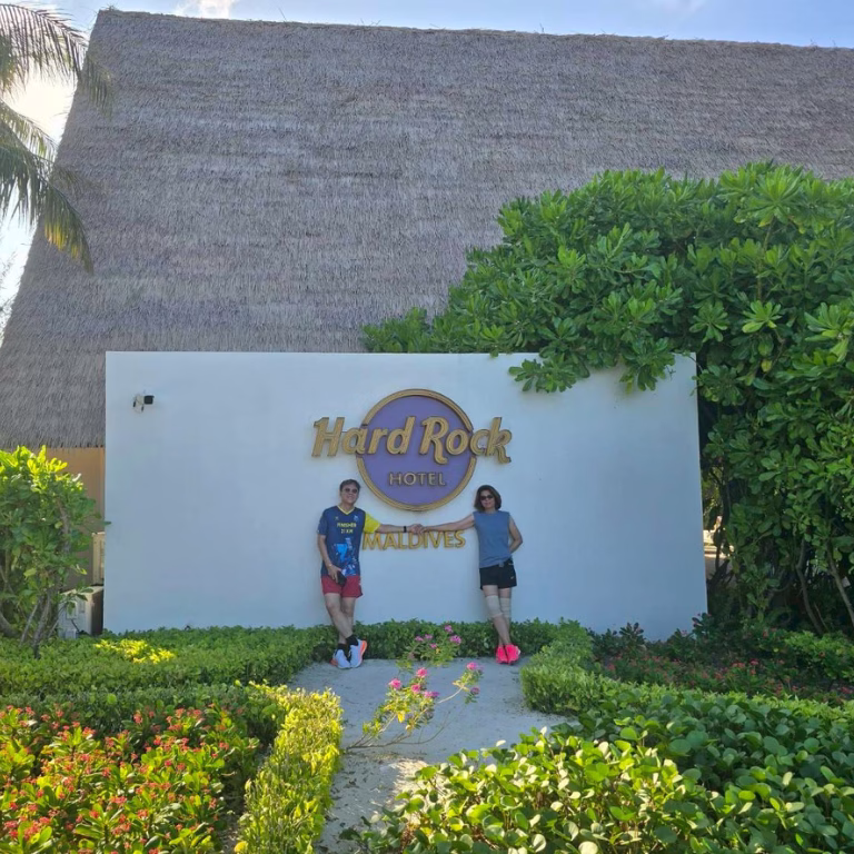 ผู้ร่วมทริปถ่ายภาพที่ระลึกบริเวณป้ายด้านหน้าโรงแรม Hard Rock Hotel Maldives ท่ามกลางบรรยากาศสวนเมืองร้อน