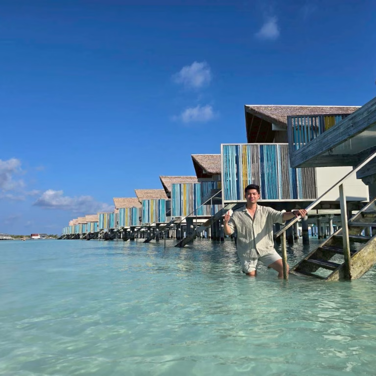 นักท่องเที่ยวถ่ายภาพที่ระลึกยืนในน้ำทะเลใสสีเทอร์ควอยซ์ บริเวณหน้าวิลลากลางน้ำ (Platinum Overwater Villa) ดีไซน์สดใสของ Hard Rock Hotel Maldives