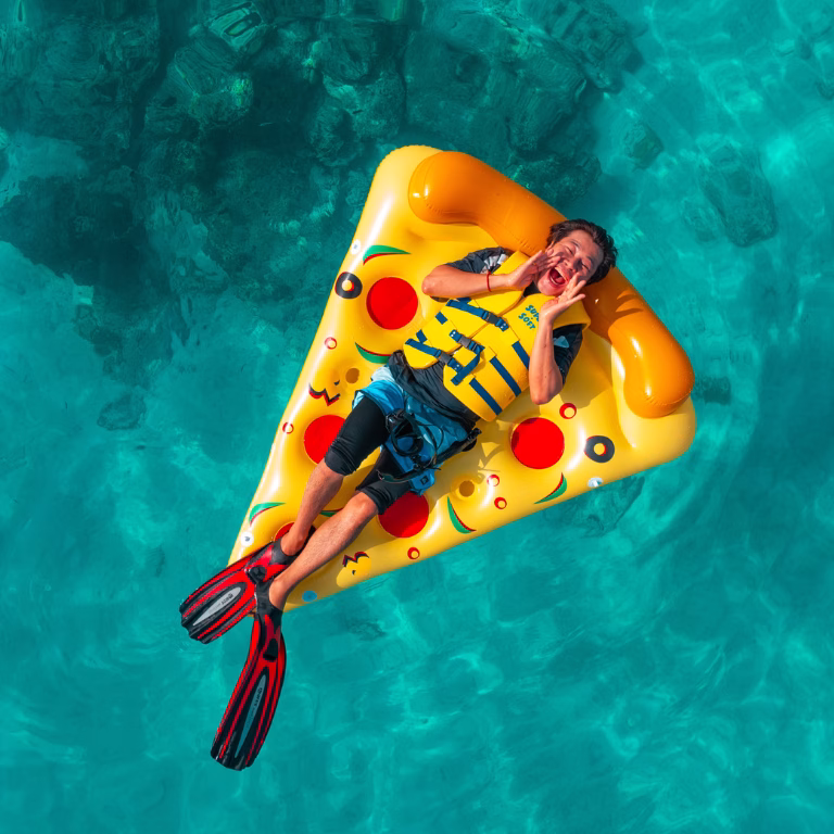 ผู้ร่วมทริปสนุกสนานกับกิจกรรมทางน้ำ ลอยตัวบนแพยางแฟนซีรูปพิซซ่าท่ามกลางน้ำใสเห็นตัวปลาที่มัลดีฟส์